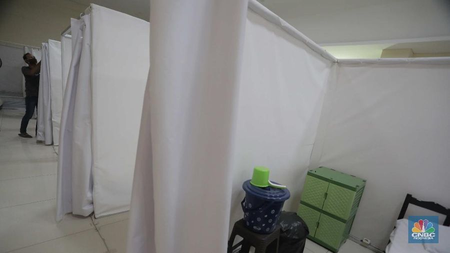 Petugas melintasi ruang isolasi mandiri pasien COVID-19 di Gelanggang Remaja Kecamatan Pademangan, Jakarta, Senin (28/9/2020). Sebanyak 30 bilik isolasi pasien Covid-19 disediakan dengan fasilitas tempat tidur, lemari, dan peralatan mandi. Gelanggang ini juga menjadi tempat percontohan graha sehat mandiri pasien Covid-19 di DKI berdasarkan kajian dari dewan riset DKI Jakarta. Meski belum diketahui pasti kapan Gelanggang Remaja Kecamatan Pademangan digunakan, prinsipnya Dispora DKI Jakarta menyiapkan fasilitas olahraga seperti Gelanggang Remaja dan GOR lainnya sebagai alternatif tempat untuk isolasi mandiri. (CNBC Indonesia/ Muhammad Sabki)