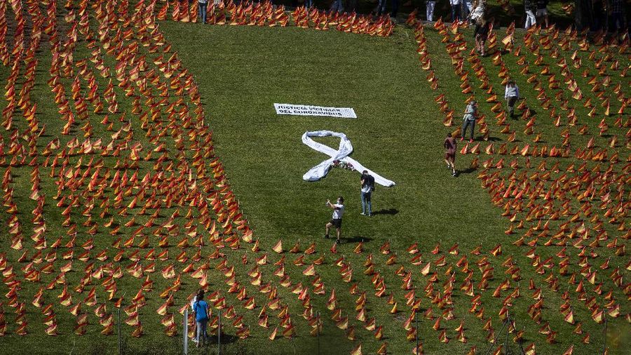A woman sits among the Spanish flags placed in memory of coronavirus (COVID-19) victims in Madrid, Spain, Sunday, Sept. 27, 2020. An association of families of coronavirus victims has planted what it says are 53,000 small Spanish flags in a Madrid park to honor the dead of the pandemic. (AP Photo/Manu Fernandez)
