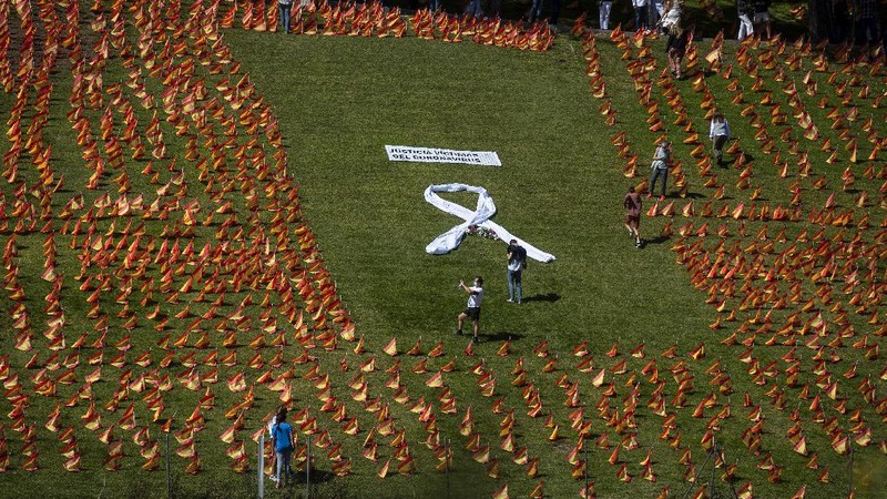 A woman sits among the Spanish flags placed in memory of coronavirus (COVID-19) victims in Madrid, Spain, Sunday, Sept. 27, 2020. An association of families of coronavirus victims has planted what it says are 53,000 small Spanish flags in a Madrid park to honor the dead of the pandemic. (AP Photo/Manu Fernandez)