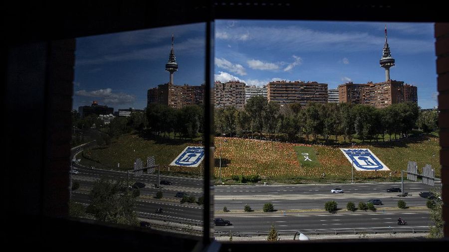 A woman sits among the Spanish flags placed in memory of coronavirus (COVID-19) victims in Madrid, Spain, Sunday, Sept. 27, 2020. An association of families of coronavirus victims has planted what it says are 53,000 small Spanish flags in a Madrid park to honor the dead of the pandemic. (AP Photo/Manu Fernandez)