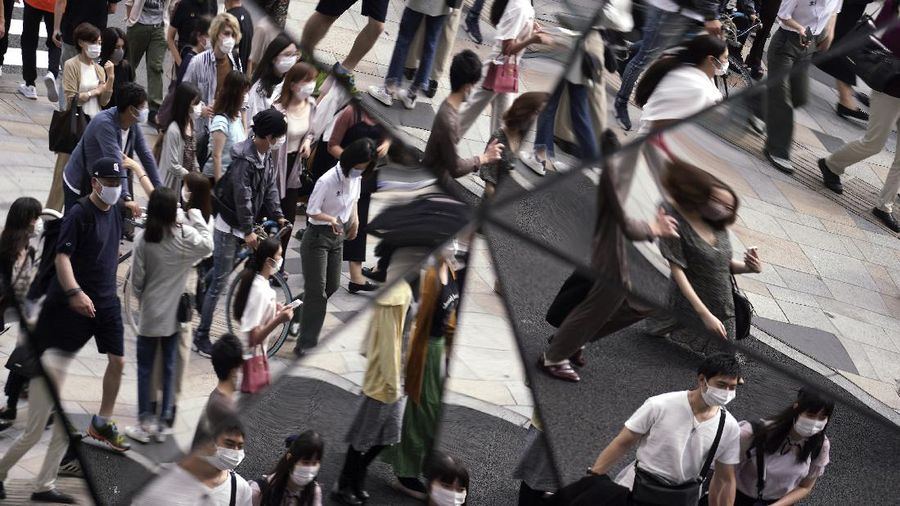 People wearing protective masks to help curb the spread of the coronavirus are reflected on mirror wall of a shopping building Monday, Sept. 21, 2020, in Tokyo. The Japanese capital confirmed more than 90 coronavirus cases on Monday marking Respect-for-the-Aged Day holiday. (AP Photo/Eugene Hoshiko)
