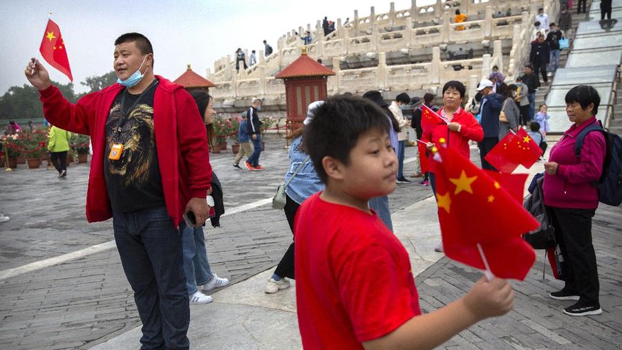 Visitors pose with Chinese flags at the Temple of Heaven in Beijing, Thursday, Oct. 1, 2020. Millions of Chinese tourists usually would use their week-long National Day holidays to travel abroad. This year, travel restrictions due to the coronavirus pandemic mean that some 600 million tourists - about 40% of the population - will travel within China during the holiday that began Thursday, according to Ctrip, China's largest online travel agency (AP Photo/Mark Schiefelbein)