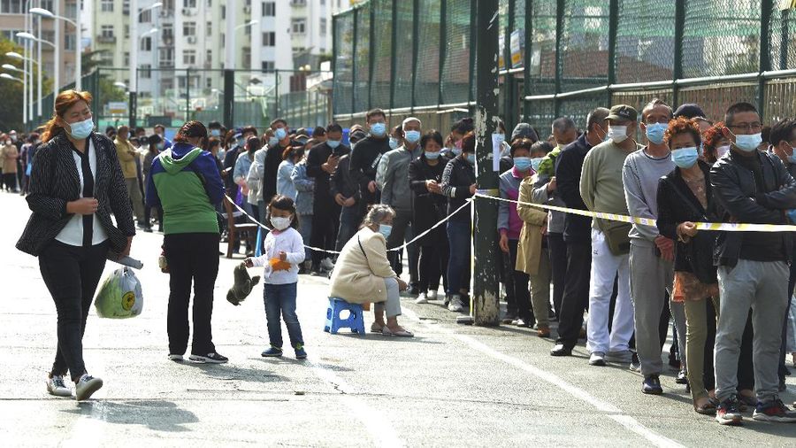 A medical staff takes a swab from a woman as residents line up for the COVID-19 test near the residential area in Qingdao in east China's Shandong province, Monday, Oct. 12, 2020. China's government says all 9 million people in the eastern city of Qingdao will be tested for the coronavirus this week after nine cases linked to a hospital were found. The announcement Monday broke a string of weeks without any locally transmitted infections reported in China. (Chinatopix via AP)