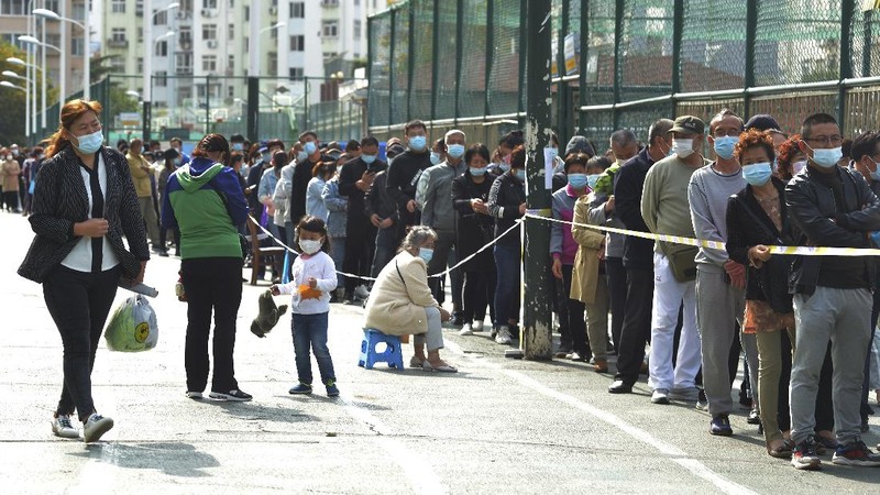 A medical staff takes a swab from a woman as residents line up for the COVID-19 test near the residential area in Qingdao in east China's Shandong province, Monday, Oct. 12, 2020. China's government says all 9 million people in the eastern city of Qingdao will be tested for the coronavirus this week after nine cases linked to a hospital were found. The announcement Monday broke a string of weeks without any locally transmitted infections reported in China. (Chinatopix via AP)