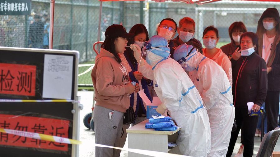 A medical staff takes a swab from a woman as residents line up for the COVID-19 test near the residential area in Qingdao in east China's Shandong province, Monday, Oct. 12, 2020. China's government says all 9 million people in the eastern city of Qingdao will be tested for the coronavirus this week after nine cases linked to a hospital were found. The announcement Monday broke a string of weeks without any locally transmitted infections reported in China. (Chinatopix via AP)