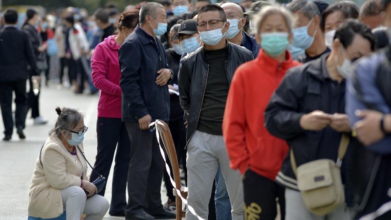A medical staff takes a swab from a woman as residents line up for the COVID-19 test near the residential area in Qingdao in east China's Shandong province, Monday, Oct. 12, 2020. China's government says all 9 million people in the eastern city of Qingdao will be tested for the coronavirus this week after nine cases linked to a hospital were found. The announcement Monday broke a string of weeks without any locally transmitted infections reported in China. (Chinatopix via AP)
