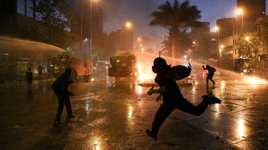 Demonstrators run as police uses water cannons to disperse them on the one-year anniversary of the start of anti-government mass protests over inequality in Santiago, Chile, Sunday, Oct. 18, 2020. (AP Photo/Esteban Felix)