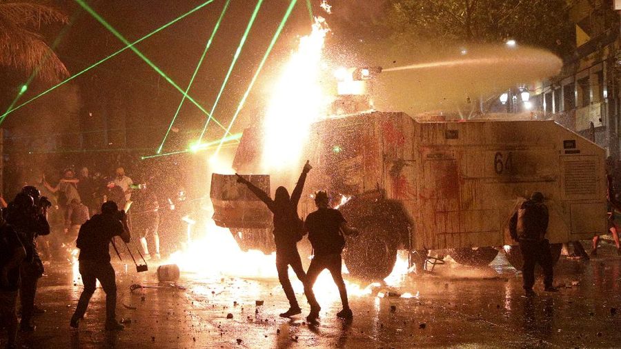 Demonstrators run as police uses water cannons to disperse them on the one-year anniversary of the start of anti-government mass protests over inequality in Santiago, Chile, Sunday, Oct. 18, 2020. (AP Photo/Esteban Felix)