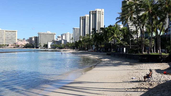 A man sits on a nearly empty Waikiki Beach in Honolulu, Friday, Oct. 2, 2020. After a summer marked by a surge of coronavirus cases in Hawaii, officials plan to reboot the tourism based economy later this month despite concerns about the state's pre-travel testing program. (AP Photo/Caleb Jones)