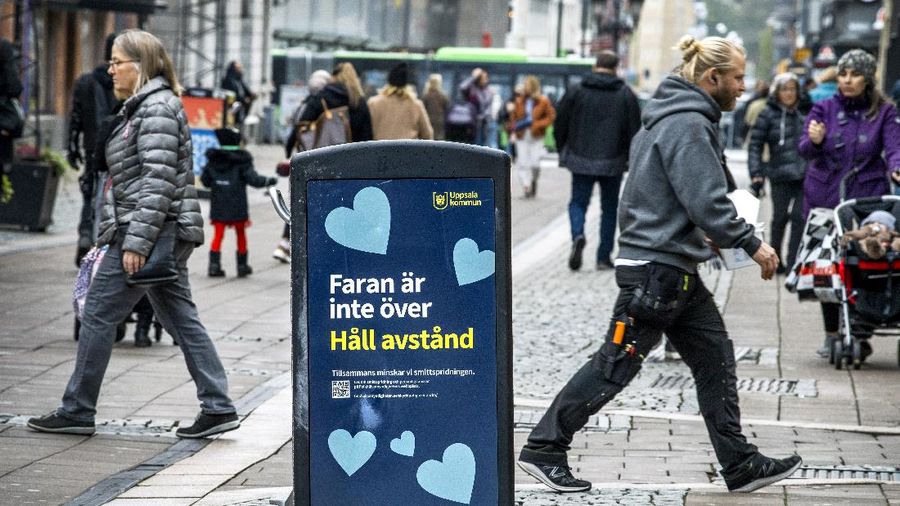 People pass a trash can with a sign reading 