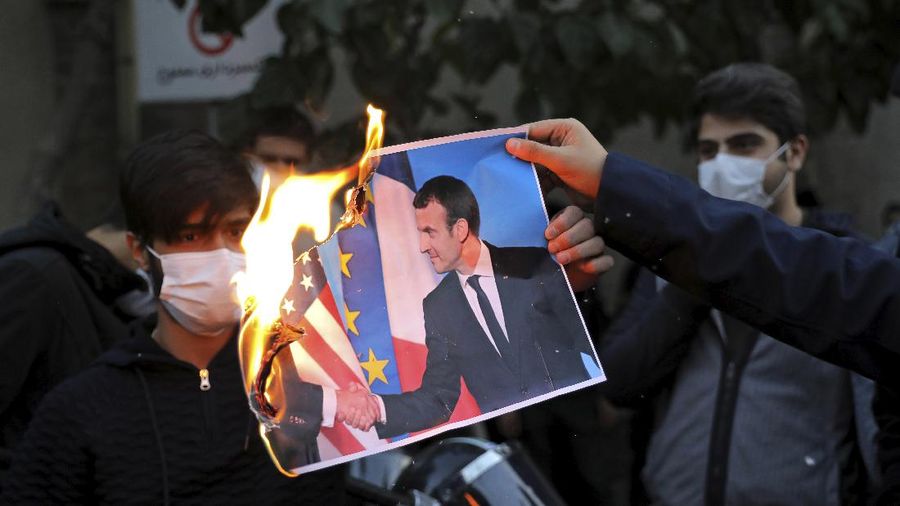 Iranian protesters hold defaced pictures of French President Emmanuel Macron during a protest against Macron and the publishing of caricatures of the Prophet Muhammad they deem blasphemous, in front of French Embassy in Tehran, Iran, Wednesday, Oct. 28, 2020. Macron has vowed his country will not back down from its secular ideals and defense of free speech. (AP Photo/Ebrahim Noroozi)