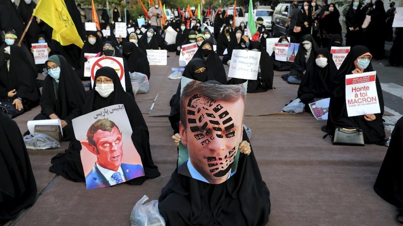 Iranian protesters hold defaced pictures of French President Emmanuel Macron during a protest against Macron and the publishing of caricatures of the Prophet Muhammad they deem blasphemous, in front of French Embassy in Tehran, Iran, Wednesday, Oct. 28, 2020. Macron has vowed his country will not back down from its secular ideals and defense of free speech. (AP Photo/Ebrahim Noroozi)