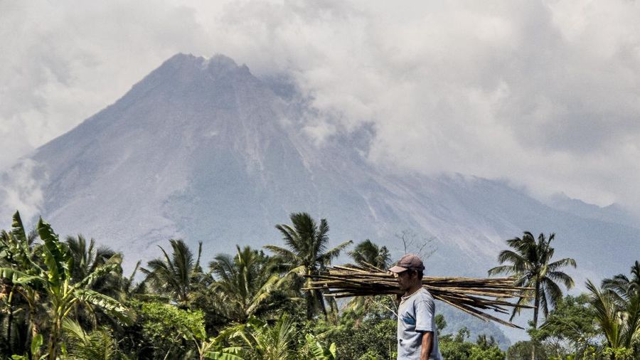 A farmer walks on his field as Mount Merapi is seen in the background in Sleman, Indonesia, Thursday, Nov. 5, 2020. Indonesian authorities raised the danger level for the volatile Mount Merapi volcano on the densely populated island of Java on Thursday and ordered a halt to tourism and mining activities. (AP Photo/Slamet Riyadi)