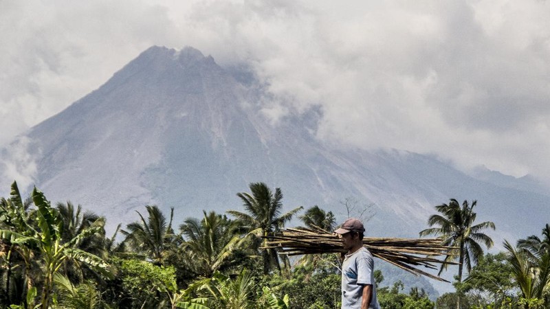 A farmer walks on his field as Mount Merapi is seen in the background in Sleman, Indonesia, Thursday, Nov. 5, 2020. Indonesian authorities raised the danger level for the volatile Mount Merapi volcano on the densely populated island of Java on Thursday and ordered a halt to tourism and mining activities. (AP Photo/Slamet Riyadi)