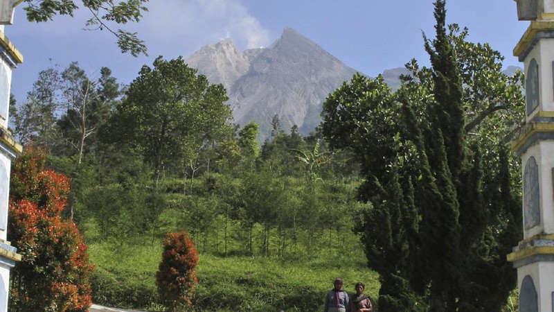 A farmer walks on his field as Mount Merapi is seen in the background in Sleman, Indonesia, Thursday, Nov. 5, 2020. Indonesian authorities raised the danger level for the volatile Mount Merapi volcano on the densely populated island of Java on Thursday and ordered a halt to tourism and mining activities. (AP Photo/Slamet Riyadi)