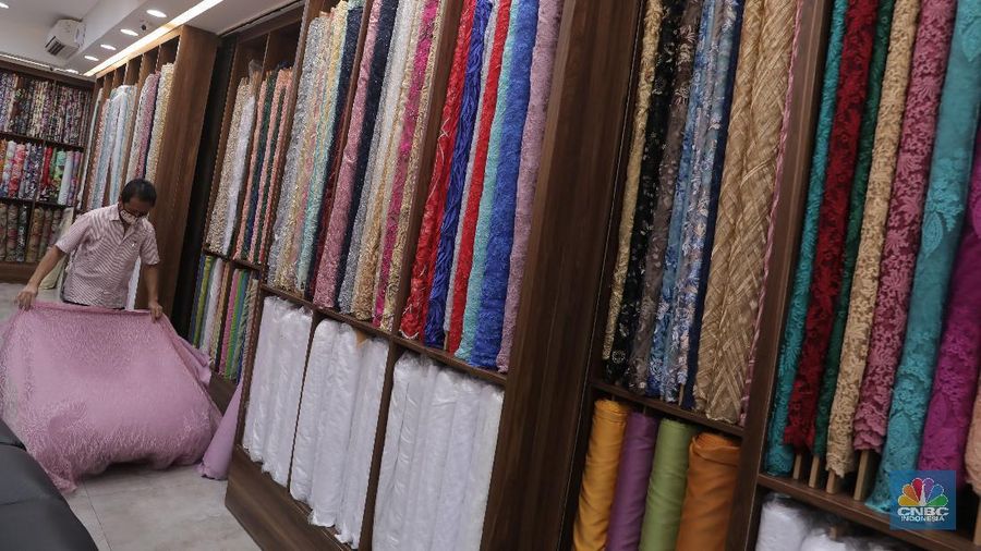 Pedagang beraktivitas di salah satu gerai kain di Pasar Mayestik, Jakarta, Rabu (11/11/2020). Pasar dalam negeri kembali dibanjiri oleh produk impor baik dalam bentuk kain maupun pakaian jadi di tengah lesunya industri domestik. Sengkarut industri tekstil terkait masalah impor masih belum berkesudahan. Saat ini ada tarik-tarikan kepentingan antara pelaku usaha industri soal mekanisme impor bahan baku yang efeknya bisa berbeda dari masing-masing industri hulu dan hilir. mengutip berita CNBC Indonesia pada 10 November, Kementerian Perdagangan dikabarkan bakal merevisi Peraturan Menteri Perdagangan (Permendag) mengenai aturan main importasi tekstil. Hal ini tidak lepas dari dorongan industri dalam negeri yang meminta adanya perubahan regulasi dari aturan-aturan yang lama. Maklum, beberapa revisi Permendag yang mengatur impor sejak tahun 2015 dinilai selalu pro barang impor. Pantauan CNBC Indonesia salah satu pemilik toko mengatakan bahwa bahan yang ia beli Grosiran di Bandung, Tasik dan sekitarnya. Namun tidak diketahui dari Mama bahan dasar tekstil itu berasal. Kalangan industri tekstil dan produk tekstil (TPT) termasuk di sektor hulu seperti benang masih mengeluhkan adanya gangguan produk impor. Masih ada persoalan tak harmoninya kebijakan sehingga ada industri yang kena dampak.  (CNBC Indonesia/Muhammad Sabki)