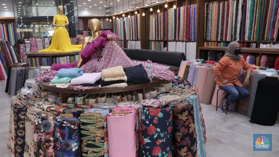 Pedagang beraktivitas di salah satu gerai kain di Pasar Mayestik, Jakarta, Rabu (11/11/2020). Pasar dalam negeri kembali dibanjiri oleh produk impor baik dalam bentuk kain maupun pakaian jadi di tengah lesunya industri domestik. Sengkarut industri tekstil terkait masalah impor masih belum berkesudahan. Saat ini ada tarik-tarikan kepentingan antara pelaku usaha industri soal mekanisme impor bahan baku yang efeknya bisa berbeda dari masing-masing industri hulu dan hilir. mengutip berita CNBC Indonesia pada 10 November, Kementerian Perdagangan dikabarkan bakal merevisi Peraturan Menteri Perdagangan (Permendag) mengenai aturan main importasi tekstil. Hal ini tidak lepas dari dorongan industri dalam negeri yang meminta adanya perubahan regulasi dari aturan-aturan yang lama. Maklum, beberapa revisi Permendag yang mengatur impor sejak tahun 2015 dinilai selalu pro barang impor. Pantauan CNBC Indonesia salah satu pemilik toko mengatakan bahwa bahan yang ia beli Grosiran di Bandung, Tasik dan sekitarnya. Namun tidak diketahui dari Mama bahan dasar tekstil itu berasal. Kalangan industri tekstil dan produk tekstil (TPT) termasuk di sektor hulu seperti benang masih mengeluhkan adanya gangguan produk impor. Masih ada persoalan tak harmoninya kebijakan sehingga ada industri yang kena dampak.  (CNBC Indonesia/Muhammad Sabki)