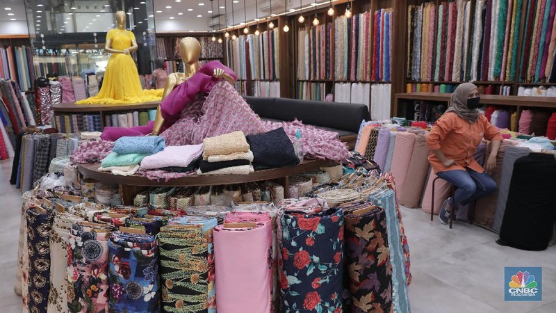 Pedagang beraktivitas di salah satu gerai kain di Pasar Mayestik, Jakarta, Rabu (11/11/2020). Pasar dalam negeri kembali dibanjiri oleh produk impor baik dalam bentuk kain maupun pakaian jadi di tengah lesunya industri domestik. Sengkarut industri tekstil terkait masalah impor masih belum berkesudahan. Saat ini ada tarik-tarikan kepentingan antara pelaku usaha industri soal mekanisme impor bahan baku yang efeknya bisa berbeda dari masing-masing industri hulu dan hilir. mengutip berita CNBC Indonesia pada 10 November, Kementerian Perdagangan dikabarkan bakal merevisi Peraturan Menteri Perdagangan (Permendag) mengenai aturan main importasi tekstil. Hal ini tidak lepas dari dorongan industri dalam negeri yang meminta adanya perubahan regulasi dari aturan-aturan yang lama. Maklum, beberapa revisi Permendag yang mengatur impor sejak tahun 2015 dinilai selalu pro barang impor. Pantauan CNBC Indonesia salah satu pemilik toko mengatakan bahwa bahan yang ia beli Grosiran di Bandung, Tasik dan sekitarnya. Namun tidak diketahui dari Mama bahan dasar tekstil itu berasal. Kalangan industri tekstil dan produk tekstil (TPT) termasuk di sektor hulu seperti benang masih mengeluhkan adanya gangguan produk impor. Masih ada persoalan tak harmoninya kebijakan sehingga ada industri yang kena dampak.  (CNBC Indonesia/Muhammad Sabki)