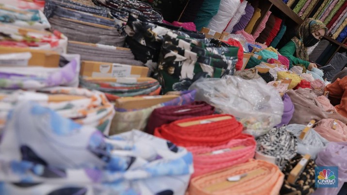 Pedagang beraktivitas di salah satu gerai kain di Pasar Mayestik, Jakarta, Rabu (11/11/2020). Pasar dalam negeri kembali dibanjiri oleh produk impor baik dalam bentuk kain maupun pakaian jadi di tengah lesunya industri domestik. Sengkarut industri tekstil terkait masalah impor masih belum berkesudahan. Saat ini ada tarik-tarikan kepentingan antara pelaku usaha industri soal mekanisme impor bahan baku yang efeknya bisa berbeda dari masing-masing industri hulu dan hilir. mengutip berita CNBC Indonesia pada 10 November, Kementerian Perdagangan dikabarkan bakal merevisi Peraturan Menteri Perdagangan (Permendag) mengenai aturan main importasi tekstil. Hal ini tidak lepas dari dorongan industri dalam negeri yang meminta adanya perubahan regulasi dari aturan-aturan yang lama. Maklum, beberapa revisi Permendag yang mengatur impor sejak tahun 2015 dinilai selalu pro barang impor. Pantauan CNBC Indonesia salah satu pemilik toko mengatakan bahwa bahan yang ia beli Grosiran di Bandung, Tasik dan sekitarnya. Namun tidak diketahui dari Mama bahan dasar tekstil itu berasal. Kalangan industri tekstil dan produk tekstil (TPT) termasuk di sektor hulu seperti benang masih mengeluhkan adanya gangguan produk impor. Masih ada persoalan tak harmoninya kebijakan sehingga ada industri yang kena dampak.  (CNBC Indonesia/Muhammad Sabki)