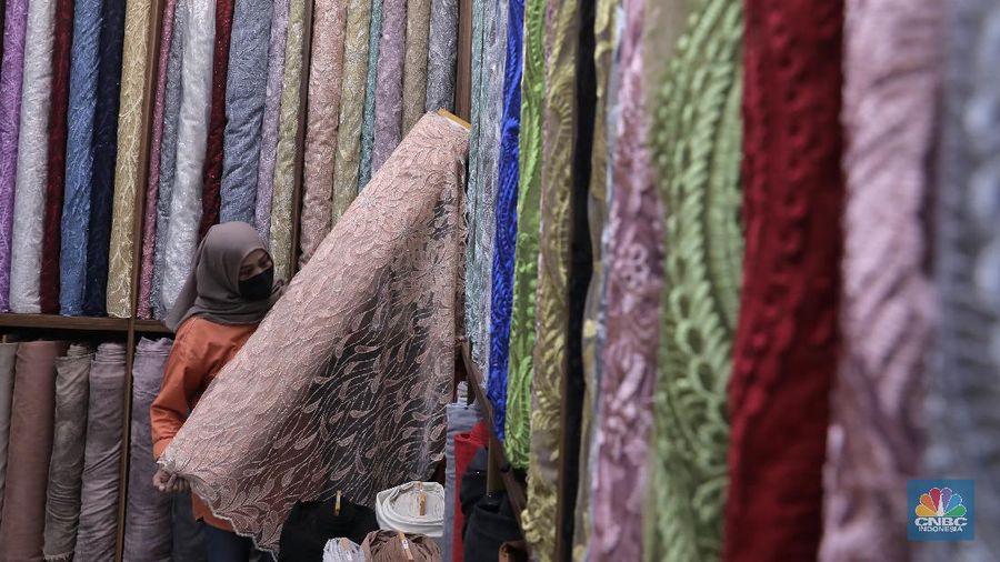 Pedagang beraktivitas di salah satu gerai kain di Pasar Mayestik, Jakarta, Rabu (11/11/2020). Pasar dalam negeri kembali dibanjiri oleh produk impor baik dalam bentuk kain maupun pakaian jadi di tengah lesunya industri domestik. Sengkarut industri tekstil terkait masalah impor masih belum berkesudahan. Saat ini ada tarik-tarikan kepentingan antara pelaku usaha industri soal mekanisme impor bahan baku yang efeknya bisa berbeda dari masing-masing industri hulu dan hilir. mengutip berita CNBC Indonesia pada 10 November, Kementerian Perdagangan dikabarkan bakal merevisi Peraturan Menteri Perdagangan (Permendag) mengenai aturan main importasi tekstil. Hal ini tidak lepas dari dorongan industri dalam negeri yang meminta adanya perubahan regulasi dari aturan-aturan yang lama. Maklum, beberapa revisi Permendag yang mengatur impor sejak tahun 2015 dinilai selalu pro barang impor. Pantauan CNBC Indonesia salah satu pemilik toko mengatakan bahwa bahan yang ia beli Grosiran di Bandung, Tasik dan sekitarnya. Namun tidak diketahui dari Mama bahan dasar tekstil itu berasal. Kalangan industri tekstil dan produk tekstil (TPT) termasuk di sektor hulu seperti benang masih mengeluhkan adanya gangguan produk impor. Masih ada persoalan tak harmoninya kebijakan sehingga ada industri yang kena dampak. (CNBC Indonesia/Muhammad Sabki)