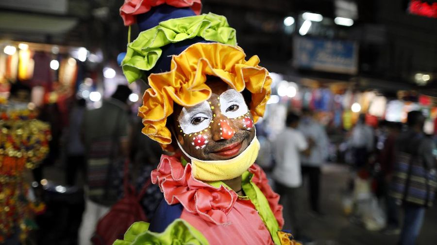 A clown smiles as he begs for alms at a crowded market place as people shop for the Hindu festival of Diwali in New Delhi, India, Saturday, Nov. 7, 2020. Diwali will be celebrated on Nov. 14. (AP Photo/Rajesh Kumar Singh)