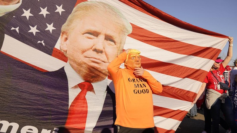 A person in a President Donald Trump mask poses for photos in front of a background with Trump on it as supporters attend pro-Trump marches, Saturday Nov. 14, 2020, in Washington. (AP Photo/Jacquelyn Martin)
