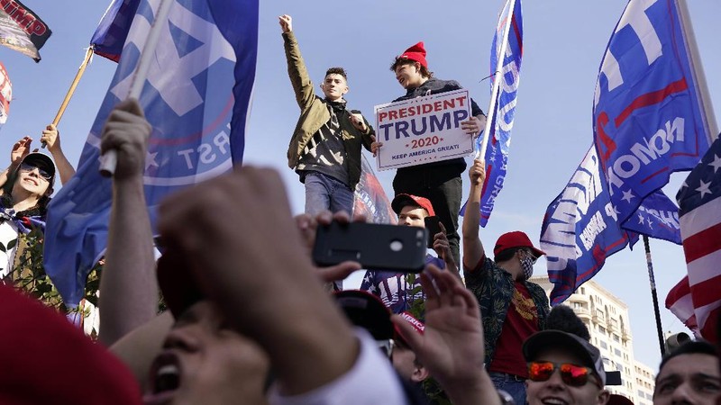 A person in a President Donald Trump mask poses for photos in front of a background with Trump on it as supporters attend pro-Trump marches, Saturday Nov. 14, 2020, in Washington. (AP Photo/Jacquelyn Martin)
