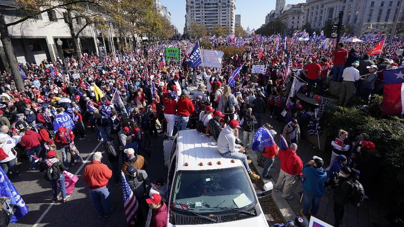 A person in a President Donald Trump mask poses for photos in front of a background with Trump on it as supporters attend pro-Trump marches, Saturday Nov. 14, 2020, in Washington. (AP Photo/Jacquelyn Martin)