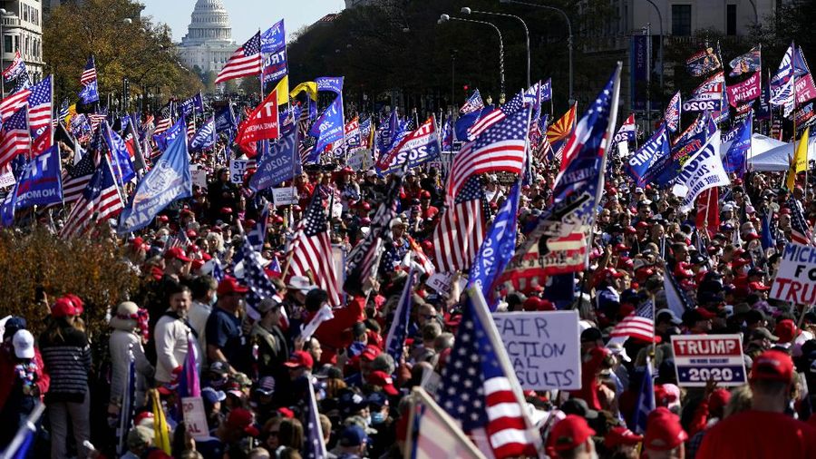 A person in a President Donald Trump mask poses for photos in front of a background with Trump on it as supporters attend pro-Trump marches, Saturday Nov. 14, 2020, in Washington. (AP Photo/Jacquelyn Martin)