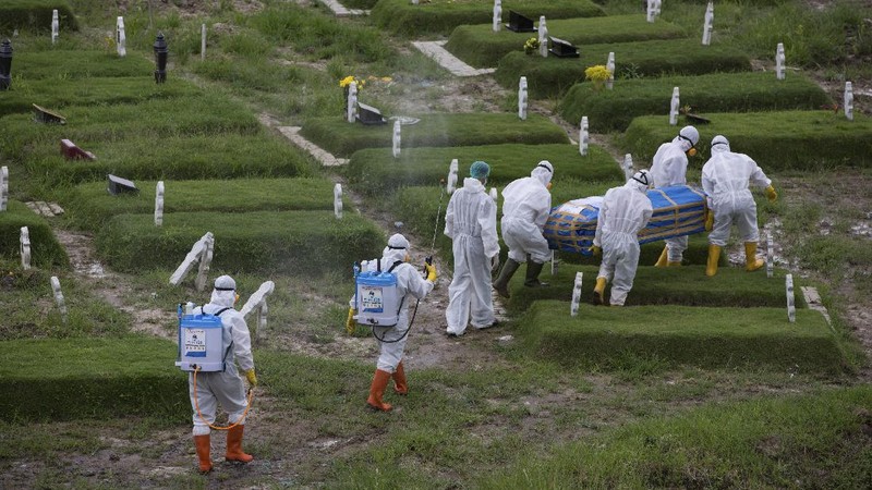 A worker sprays a colleague with disinfectant after a burial of someone who presumably died of the coronavirus at a cemetery in Medan, North Sumatra, Indonesia, Tuesday, Nov. 24, 2020.(AP Photo/Binsar Bakkara)