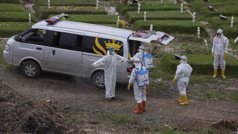A worker sprays a colleague with disinfectant after a burial of someone who presumably died of the coronavirus at a cemetery in Medan, North Sumatra, Indonesia, Tuesday, Nov. 24, 2020.(AP Photo/Binsar Bakkara)