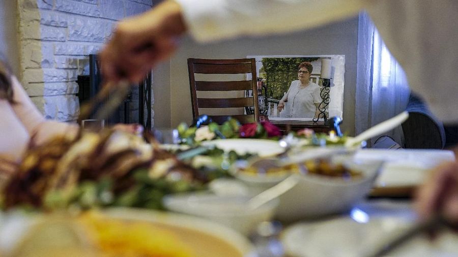 An image Ana Martinez, the recently deceased mother of sisters Vivian Zayas and Alexa Rivera, rests besides an empty chair as Thanksgiving dinner is served, Thursday, Nov. 26, 2020, in Deer Park, N.Y. Ana Martinez died at 78 on April 1 while recovering at a nursing home from a knee replacement. The family is having their traditional meal of turkey, yams, green beans and rice and beans — but Zayas is removing a seat from the table at her home in Deer Park, New York, and putting her mother's walker in its place. (AP Photo/John Minchillo)