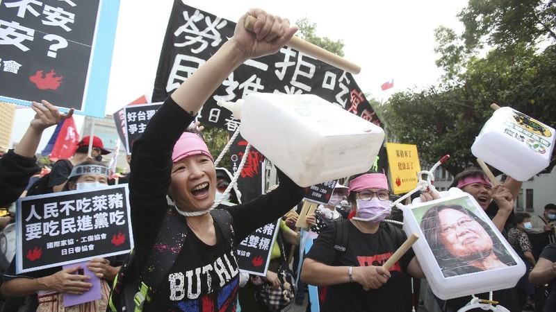 In this image made from video, Taiwanese Premier Su Tseng-chang holds a microphone as opposition party lawmakers from the Nationalist party (KMT) block his attempt to speak during a parliament session in Taipei, Taiwan, Friday, Nov. 27, 2020. Taiwan's lawmakers got into a fist fight and threw pig guts at each other Friday over a soon-to-be enacted policy that would allow imports of U.S. pork and beef. The banner at right reads: “Democratic Progressive Party feeds people with ractopamine pork.” (FTV via AP)