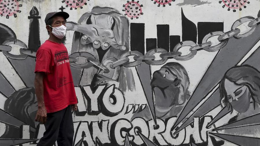 A man wearing face mask walks past a coronavirus-themed mural in Jakarta, Indonesia, Wednesday, Nov. 25, 2020. Writings on the mural read 