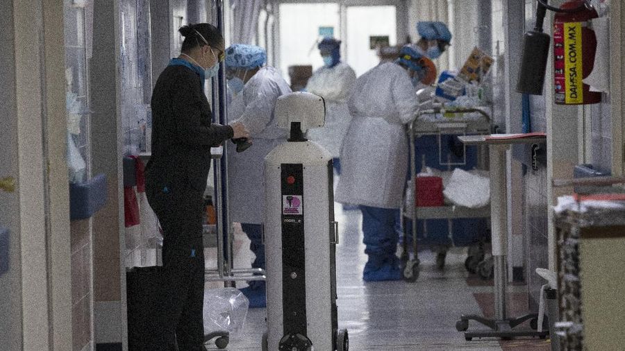 A healthcare worker communicates with a fellow doctor via Laluchy Robotina, a robot designed to aid in the mental health of patients infected with the new coronavirus, in the COVID-19 ward at 20 de November National Medical Center in Mexico City, Friday, Sept. 25, 2020. The 1.4-meter-tall robot that moves around on wheels visiting COVID-19 patients, is equipped with a camera and display screen which allows the patients to visit with relatives and to also communicate with healthcare workers, helping to reduce the risk of infection. (AP Photo/Marco Ugarte)