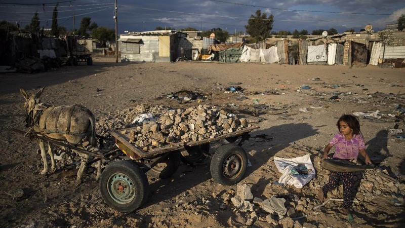 A Palestinian girl walks next to a donkey carte loaded with rocks in a slum on the outskirts of Khan Younis Refugee Camp, in the southern Gaza Strip, Wednesday, Nov. 25, 2020. Israel's blockade of the Hamas-ruled Gaza Strip has cost the seaside territory as much as $16.7 billion in economic losses and caused its poverty and unemployment rates to skyrocket, a U.N. report said Wednesday, as it called on Israel to lift the 13-year closure. (AP Photo/Khalil Hamra)