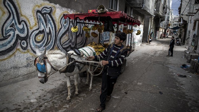 A Palestinian girl walks next to a donkey carte loaded with rocks in a slum on the outskirts of Khan Younis Refugee Camp, in the southern Gaza Strip, Wednesday, Nov. 25, 2020. Israel's blockade of the Hamas-ruled Gaza Strip has cost the seaside territory as much as $16.7 billion in economic losses and caused its poverty and unemployment rates to skyrocket, a U.N. report said Wednesday, as it called on Israel to lift the 13-year closure. (AP Photo/Khalil Hamra)