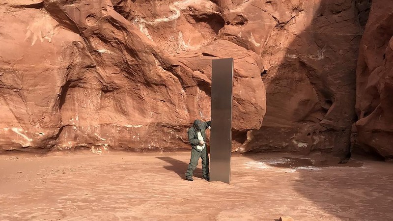 FILE - In this Nov. 18, 2020, file photo provided by the Utah Department of Public Safety, a Utah state worker stands next to a metal monolith in the ground in a remote area of red rock in Utah. The mysterious silver monolith that was placed in the Utah desert has disappeared less than 10 days after it was spotted by wildlife biologists performing a helicopter survey of bighorn sheep, federal officials and witnesses said. The Bureau of Land Management said it had received credible reports that the three-sided stainless steel structure was removed on Nov. 27.  (Utah Department of Public Safety via AP, File)
