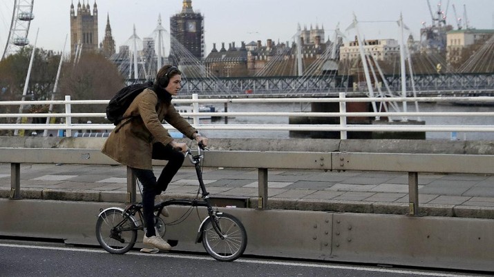A man cycles on a Brompton folding bicycle over Waterloo Bridge backdropped by the scaffolded Houses of Parliament and Elizabeth Tower, known as Big Ben, during England's second coronavirus lockdown, in London, Friday, Nov. 20, 2020. The team at Brompton Bicycles company thought they were prepared for Britain's Brexit split with Europe, but they face uncertainty about supplies and unexpected new competition from China, all amid a global COVID pandemic. (AP Photo/Matt Dunham)