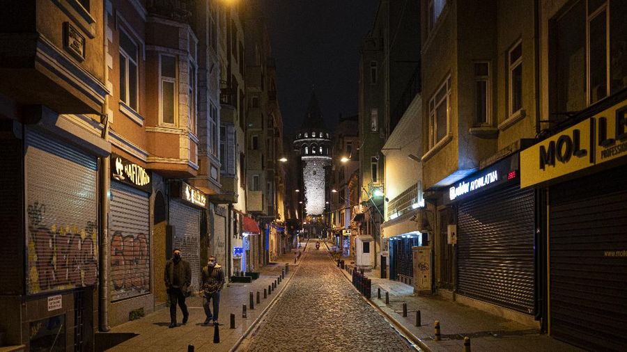 People walk in Istanbul, backdropped by the Galata Tower, during a curfew Tuesday, Dec. 1, 2020, part of the new measures to try curb the spread of the coronavirus. Turkey had gone into the most widespread lockdown so far amid a surge in COVID-19 infections, extending curfews to weeknights and full lockdowns over weekends. The curfew would be implemented on weekdays between 9:00 pm and 5:00 am. He also announced total weekend lockdowns from 9:00 pm on Friday evenings to 5:00 am Monday. (AP Photo)