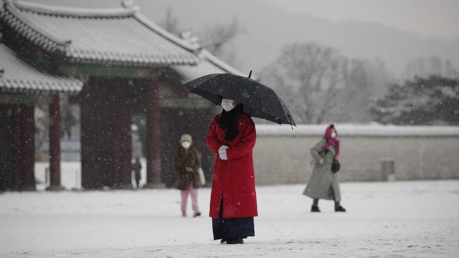 An employee wearing a face mask as a precaution against the coronavirus uses an umbrella to take shelter from the snow at the Gyeongbok Palace, one of South Korea's well-known landmarks, in Seoul, South Korea, Sunday, Dec. 13, 2020. (AP Photo/Lee Jin-man)