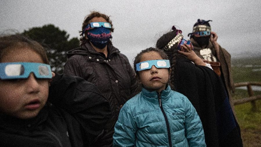 A Mapuche Indigenous family uses special glasses to try and observe a total solar eclipse in Carahue, La Araucania, Chile, Monday, Dec. 14, 2020. The total eclipse was barely visible from Carahue because of an overcast sky. (AP Photo/Esteban Felix)