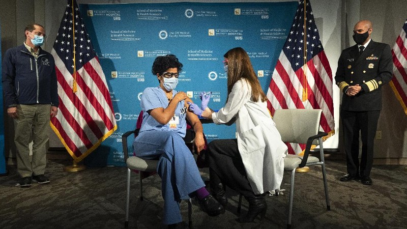 Health and Human Services Secretary Alex Azar, at left, and U.S. Surgeon General Dr. Jerome Adams, far right, watch as Dr. Sheetal Sheth, center left, OB-GYN and Medical Director for Labor and Delivery at George Washington University Hospital, is vaccinated for COVID-19 by nurse Lillian Wirpsza, Monday, Dec. 14, 2020, in Washington. (AP Photo/Jacquelyn Martin, Pool)
