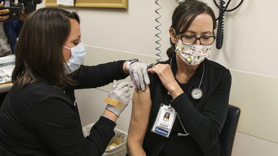 Health and Human Services Secretary Alex Azar, at left, and U.S. Surgeon General Dr. Jerome Adams, far right, watch as Dr. Sheetal Sheth, center left, OB-GYN and Medical Director for Labor and Delivery at George Washington University Hospital, is vaccinated for COVID-19 by nurse Lillian Wirpsza, Monday, Dec. 14, 2020, in Washington. (AP Photo/Jacquelyn Martin, Pool)