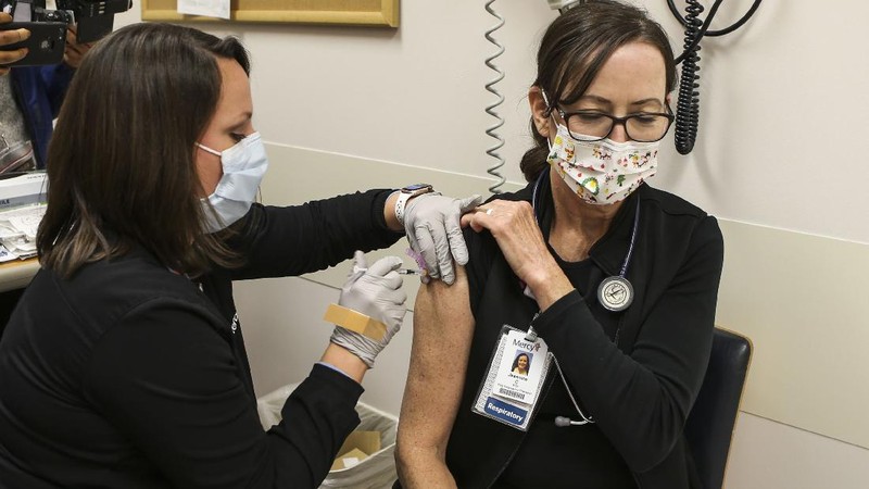 Health and Human Services Secretary Alex Azar, at left, and U.S. Surgeon General Dr. Jerome Adams, far right, watch as Dr. Sheetal Sheth, center left, OB-GYN and Medical Director for Labor and Delivery at George Washington University Hospital, is vaccinated for COVID-19 by nurse Lillian Wirpsza, Monday, Dec. 14, 2020, in Washington. (AP Photo/Jacquelyn Martin, Pool)