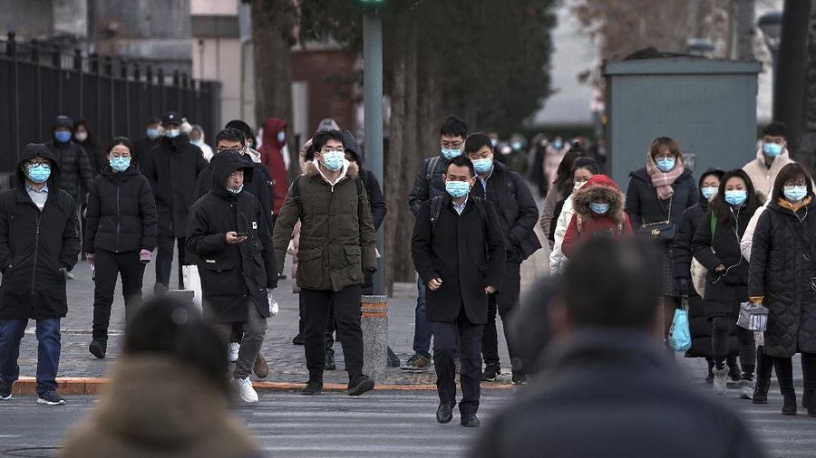 People wearing face masks to help curb the spread of the coronavirus walk across a street as they head for work during the morning rush hour in Beijing, Tuesday, Dec. 15, 2020. (AP Photo/Andy Wong)