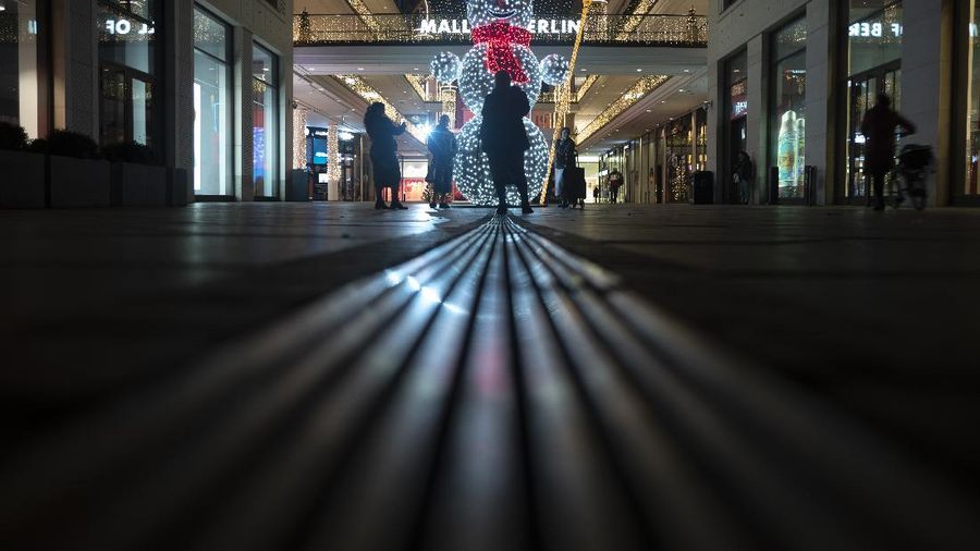 People take photos in front of an illuminated Snowman in the deserted entrance of the 'Mall of Berlin' shopping center late afternoon in Berlin, Germany, Wednesday, Dec. 16, 2020. Germany has entered a harder lockdown, closing most of shops shops and schools in an effort to bring down stubbornly high new cases of the coronavirus.(AP Photo/Markus Schreiber)