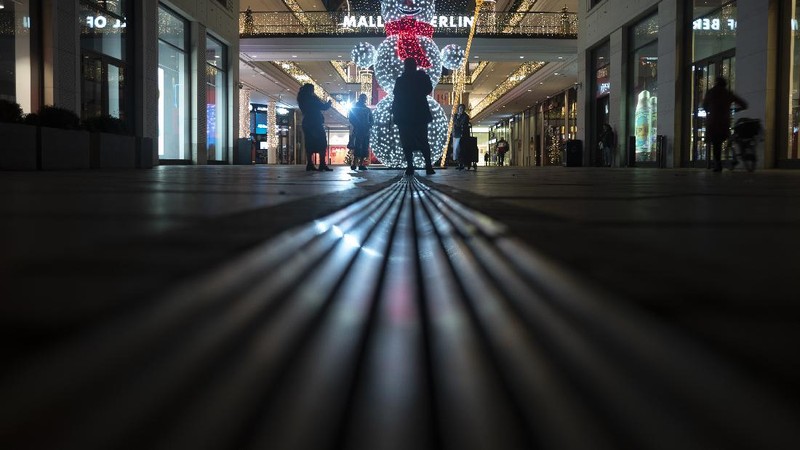 People take photos in front of an illuminated Snowman in the deserted entrance of the 'Mall of Berlin' shopping center late afternoon in Berlin, Germany, Wednesday, Dec. 16, 2020. Germany has entered a harder lockdown, closing most of shops shops and schools in an effort to bring down stubbornly high new cases of the coronavirus.(AP Photo/Markus Schreiber)