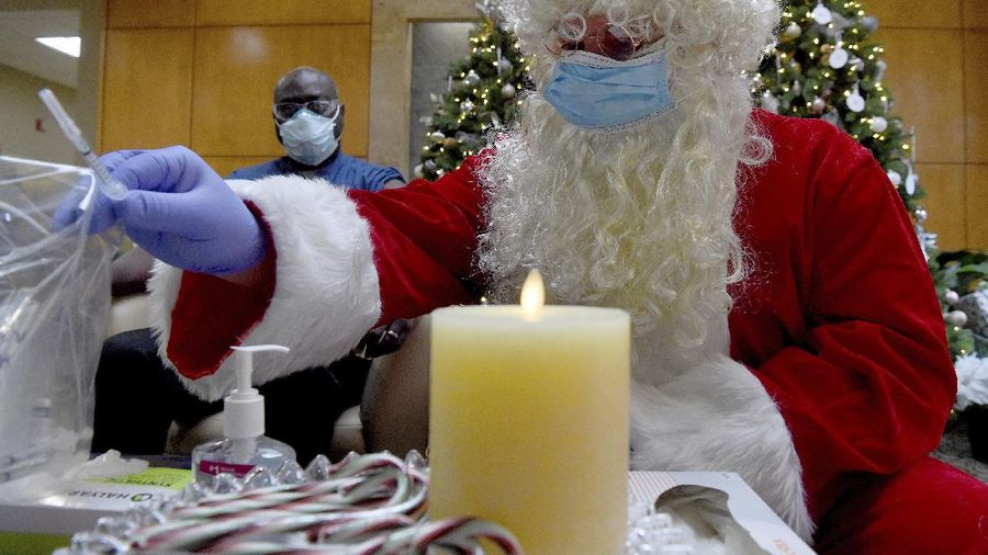 Santa, Robert Carroll, M.D., an Emergency Medicine Specialist with Manchester Memorial Hospital, takes a syringe from the plastic bag with already prepared dosages of the Pfizer-BioNTech vaccine, to be administered to Marvin Bristol, rear, a respiratory therapist and a front-line healthcare worker, Wednesday, Dec. 16, 2020, in Manchester, Conn. (Jim Michaud/Journal Inquirer via AP)