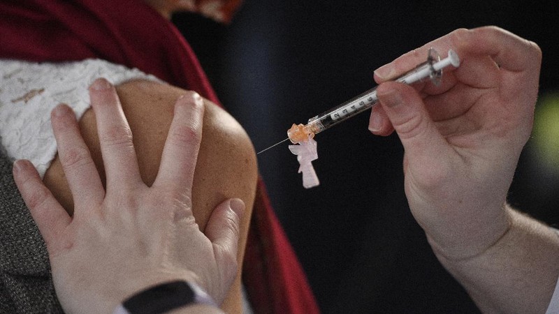 Santa, Robert Carroll, M.D., an Emergency Medicine Specialist with Manchester Memorial Hospital, takes a syringe from the plastic bag with already prepared dosages of the Pfizer-BioNTech vaccine, to be administered to Marvin Bristol, rear, a respiratory therapist and a front-line healthcare worker, Wednesday, Dec. 16, 2020, in Manchester, Conn. (Jim Michaud/Journal Inquirer via AP)